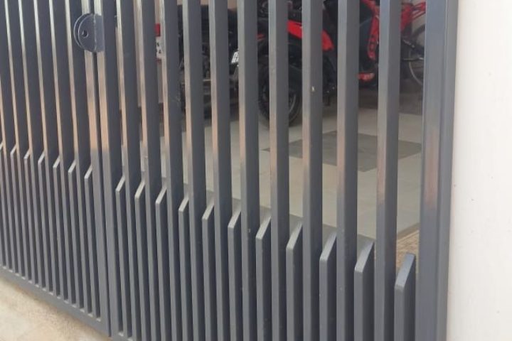 Portón gris de perfiles verticales instalado en la cochera de una casa