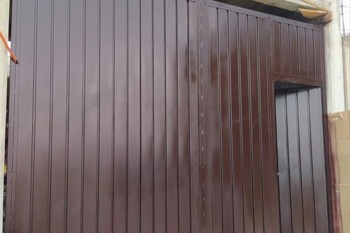 Portón café de lámina acanalada con puerta peatonal integrada, recién instalado en obra
